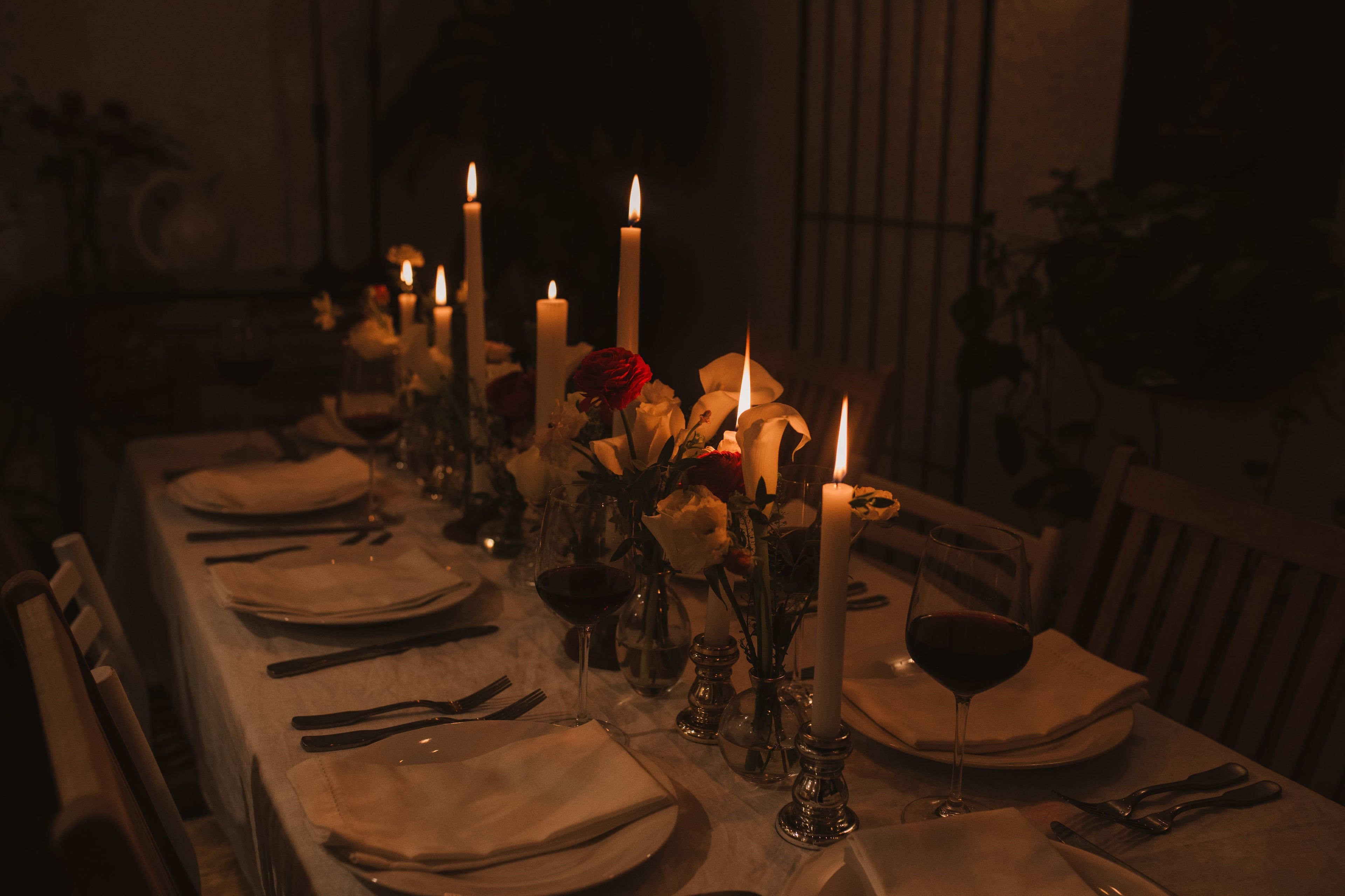 A dining table set with candles and flowers and a few glasses of wine. 