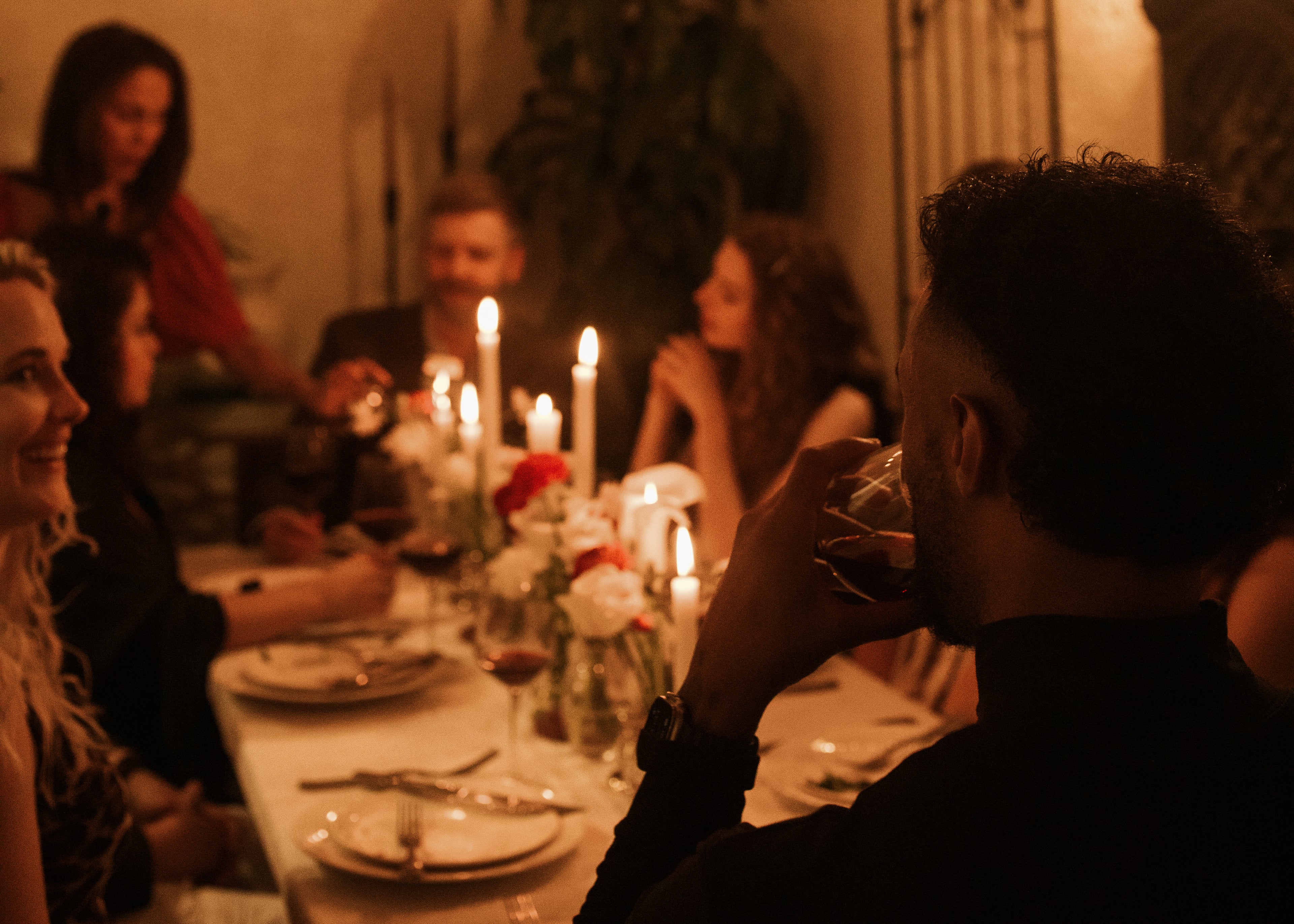 A group of well-dressed individuals sharing a candlelit dinner at an elegant table, set with flowers, wine glasses, and plates, creating a warm and intimate atmosphere for connection.